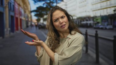Genç İspanyol kadın, binalarla dolu kalabalık bir şehir sokağında sorgulama jesti olarak çıplak ellerini uzatıyor..