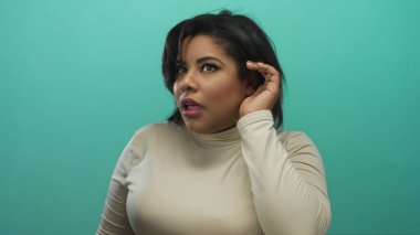 Katı yeşil arka planda dikkatle dinleyen bir kadın, merakını ve dikkatini gösteriyor..