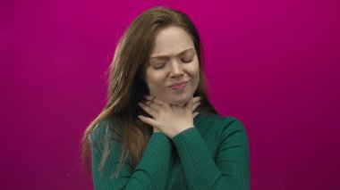 Beyaz bir kadın, pembe bir stüdyo duvarına karşı suratını buruşturarak acı çektirmek için el ele tutuşuyor..