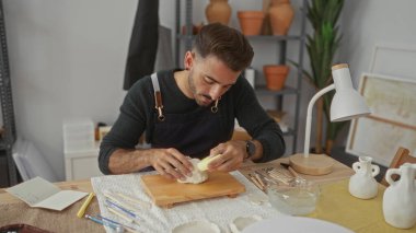 Stüdyoda beyaz çamuru çıplak elle şekillendiren İspanyol genç adam. Konsantrasyon yaratıcılığı..