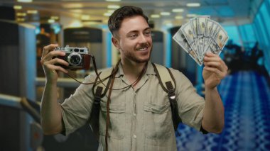Spor salonunda gülümseyen ve fotoğrafçılıktan zevk alan kameralı genç bir adam Amerikan parası ve seyahat macerası sergiliyor..