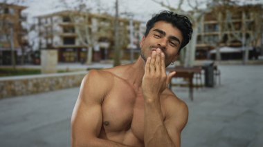 Kapalı gözlerle gülümseyen gömleksiz bir adam omuzlarını tutar ve sokakta çıplak göğsünü gösterir; memnuniyet.