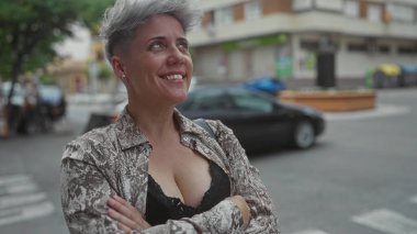 Çapraz kollu bir kadın şehir caddesinde zebra sınırını geçerken çıplak göğüs dekoltesi ve gümüş küpeler gösteriyor..