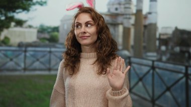 Tavşan kulaklı genç bir kadın tarihi Roma harabelerinin yanında gülümsüyor, süveter giyiyor, arka planda Roma mimarisi, eğlence ve tarihi harmanlıyor..