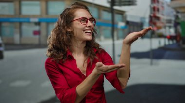 Şehirli bir kadın, açık havada kırmızı tişörtlü, güler yüzlü güneşli bir günde arka planda geziyor..