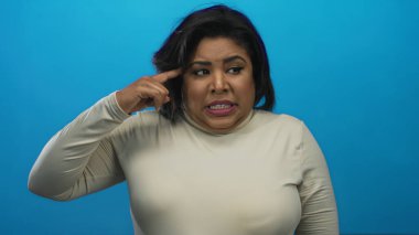 Latin büyük boy kadın mavi duvara karşı çılgınca jest yapıyor, mizah ve duyguyu canlı bir şekilde aktarıyor..