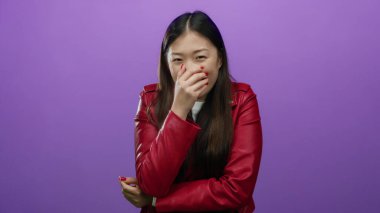 Kırmızı ceketli bir kadın gülüyor, ağzı kapalı, mor arka planda neşeli duygular besliyor, çekici bir moda..