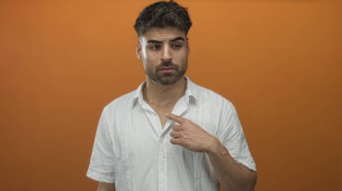 Parmakla göğsünü gösteren turuncu stüdyo ışıkları ve tarafsız yüz ifadesi olan bir adam..