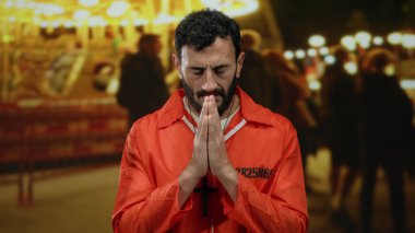 Turuncu tulumlu İspanyol bir mahkum, sakallı bir panayır atlıkarıncasında dua ediyor, neşeli bir şenlik ortamı ile yan yana hapsediliyor..