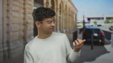 Güneşli tarihi bir caddede çıplak elle gitar çalan gözlüklü bir adam..