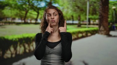 Arka planda yeşil ağaçlar olan açık hava parkında neşeli ruh hali sergileyen bir kadın..