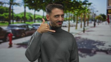 Balıkçı yaka kazak giyen adam, park halindeki arabalarla dolu bir caddede parmağını öne uzatıyor..