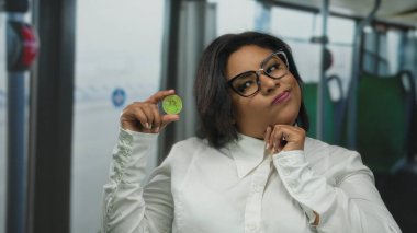 Kadın, şehir ortamında otobüs sergisi kripto para biriminde dijital finans kavramlarını vurgulayan düşünceli bir ifadeyle Bitcoin tutuyor.