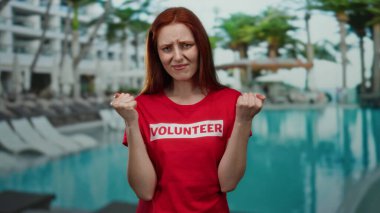 Kızıl saçlı kadın bir tatil köyünde havuz başında kırmızı gönüllü gömlekli duygularını hissediyor..