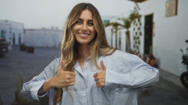 Sarışın kadın, kırsal bir avluda iki eliyle baş parmak işareti gösteriyor. Onaylama iyimserliği..