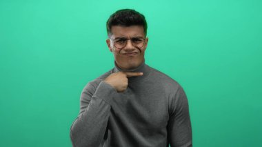 Genç adam canlı yeşil bir arka planda, gözlükleriyle güven içinde el kol hareketi yaparak, izole edilmiş, modern ve şık bir portre çiziyor..