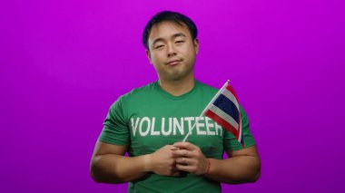 Yeşil gönüllü Asyalı genç adam pembe arka planda Tayland bayrağı tutuyor.