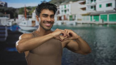 Genç İspanyol adam, güneşli bir deniz kenarında geniş bir gülümseme ile elleri ile kalp şekli oluşturur; sıcak sevgi.