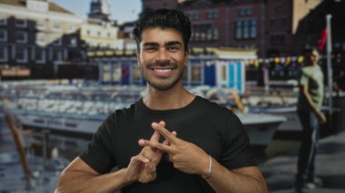 İspanyol asıllı genç adam hareketli bir limanda limanda limanlı bir yatın yanında hashtag jesti yapıyor; sosyal medya bağlantısı mutluluğu.