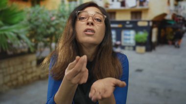 Orta yaşlı İspanyol kadın, şehir caddesinde avuç içi açık ve parmağıyla göğsü göğse gösteren hareketler yapıyor..