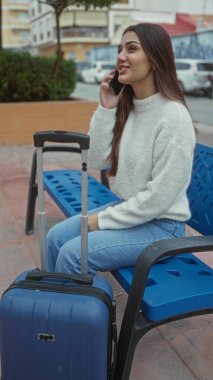 Bankta oturan bir kadın, şehir sokağında çantasıyla telefonda konuşuyor, günlük seyahat ve İspanyol tarzı gösteriş yapıyor..