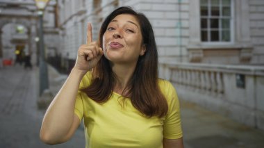 Orta yaşlı kadın parmaklarını yukarı kaldırarak gülümsüyor; merak merak uyandırıcı iyimserlik.