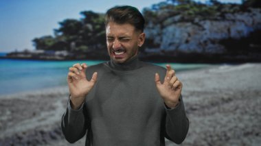 Parlak güneş altındaki kayalık sahil kayalıklarının yakınındaki kumsalda yüzünü buruşturan ve işaret eden adam hayal kırıklığı.