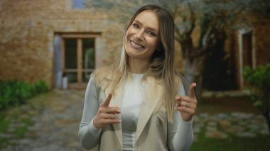Bir kadın gülerek şehir caddesinde gün ışığında taş binalarla kamerayı işaret ediyor..