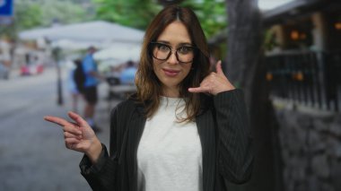 Genç bir kadın canlı şehir merkezindeki sokak kafesi terasına işaret ederken çağrı işareti yapıyor..