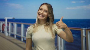 Yolcu teknesindeki kadın, başparmağıyla güvenle gülümsüyor, sarışın saçlar berrak gökyüzünün altında berrak mavi denizlere doğru akıyor, neşe ve macera taşıyor..