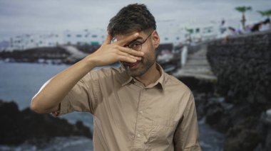 Taş iskele yolundaki kayalık bir sahil binasının yanındaki bej gömlekli İspanyol adam gözlerini kapatıyor. Yalnızlık yansıması..