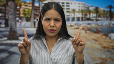 Sahilde kamerayı gösteren parmaklarını kaldıran kadın, deniz kenarındaki gezinti alanında Latin kökenli genç bir Latin tavır sergiliyor..