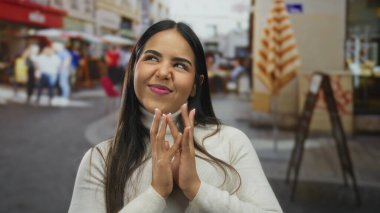 Kendine güveni tam bir kadın, neşeli bir caddede entrika çevirirken ellerini bir araya getiriyor. Genç Latin bir şahsiyet açık havada muzip, gülümseyen bir ifadeyle duruyor..