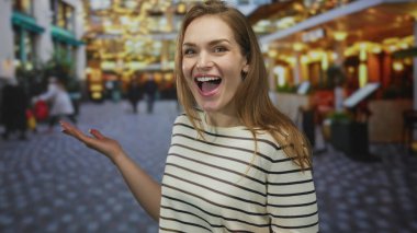 Çizgili bluzlu genç kadın gülümsüyor ve meşgul caddede parlayan kafenin ışıkları altında parmak ucuyla işaret ediyor; heyecan.