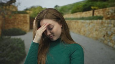 Açık hava binasının girişinde alnına kadar yeşil kazak giyen genç bir kadın. Stres bunalımı..