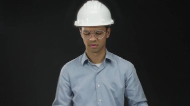 Beyaz başlık takan ve gözlük takan adam stüdyoda büyük planlar okuyor..