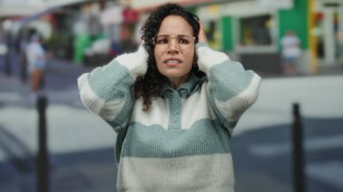 Çizgili kazaklı genç İspanyol kadın kalabalık bir sokakta kafası karışmış, elleri havada el kol geziyor, canlı bir şehir ortamında belirsizlik ve merak taşıyor..