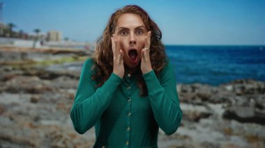 Kayalık bir sahil kenarında, berrak bir gökyüzünün altında canlı bir mavi denizle duygularını ifade eden bir kadın, açık havada genç bir neşe yakalıyor..