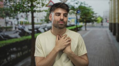 Elleri göğsüne ve gözlerine çapraz olan Latin asıllı genç adam şehir sokaklarında nazikçe kapanıyor..