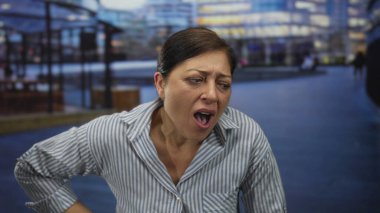 İspanyol orta yaşlı kadın, arkasında bulanık şehir binalarıyla sokakta sırt üstü yatıyor; sırt ağrısı rahatsızlığı.