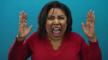 Kırmızı bir kazak giyen, çeşitli kadın enerjisi ve duygularını somutlaştıran, mavi izole bir arka plan önünde ellerini kaldırarak heyecanını ifade eden bir kadın..