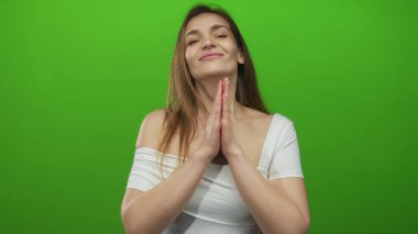 Beyaz omuzlu kadın, stüdyoda ellerini birbirine kenetledi. Arkaplanda yeşil bir perde vardı..
