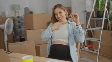 Elinde anahtar olan hamile kadın, yeni dairesinde kutluyor. Kutuları taşıyarak, evin içinde neşe ve beklenti içinde..