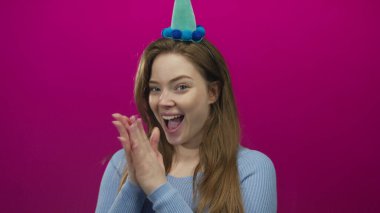 Keçeli şapka giyen kadın parti şapkasını işaret ediyor ve stüdyoda geniş bir şekilde gülümsüyor; doğum günü kutlaması neşesi.