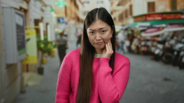 Pembe kazaklı, uzun saçlı bir kadın Çin 'de bulanık insanlarla dolu kalabalık bir caddede düşünceli ve düşünceli görünüyor..