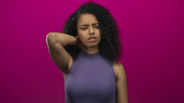 Boyun ağrısından muzdarip bir kadın canlı pembe bir arka planın önünde duruyor ve bir rahatsızlık ve gerilim anı yakalıyor..