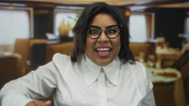 Kendine güveni tam, gözlüklü genç bir kadın restoranda gülümsüyor, zarafet ve tarz sergiliyor..