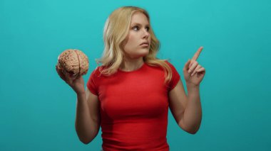 Beyni tutan, kırmızı gömlekli, mavi arkaplana karşı düşünceli, sarı saçlı, zeki, bilim, eğitim, sağlık, odaklanma, anlayış kavramını merak eden bir kadın..