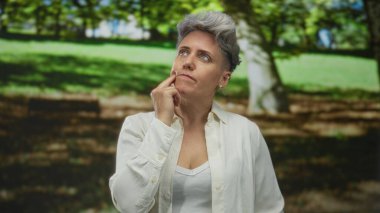 Kısa saçlı, beyaz gömlekli bir kadın, hafif kaşları çatık ve gözleri kapalı olarak el ele tutuşuyor..