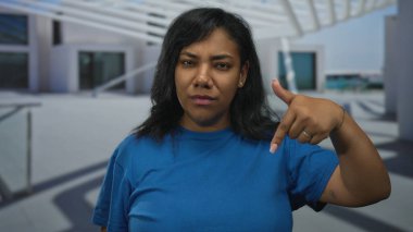 Mavi gömlekli kadın, ciddi bir ifadeyle şehir caddesinde iki parmağını da binanın önünde gösteriyor..